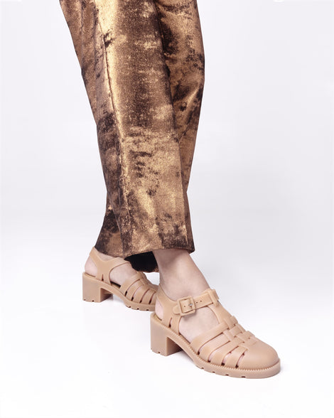 Model's legs in brown pants wearing a pair of beige Possession Heel women's fisherman style sandals.