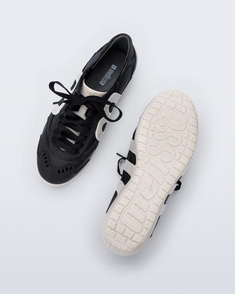 Top and bottom view of a pair of black Motion sneakers with white colored sole and M monogram on side