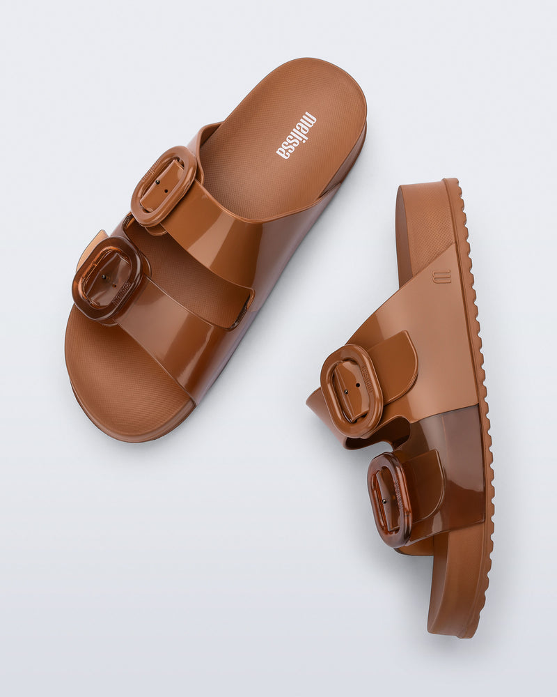 Side and top view of a pair of brown Cozy slides with part clear brown upper with 2 buckles