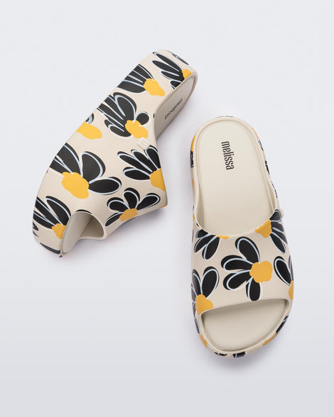 Side and top view of a pair of beige Free Print Platform slides with a black and yellow flower print.
