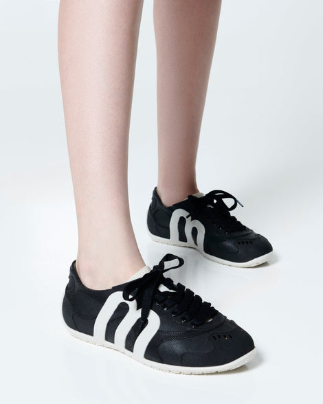 Model's legs wearing a pair of black Motion sneakers with white colored sole and M monogram