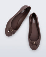 An angled top view of a pair of brown Melissa flats with a bow detail with gold accents on the bow