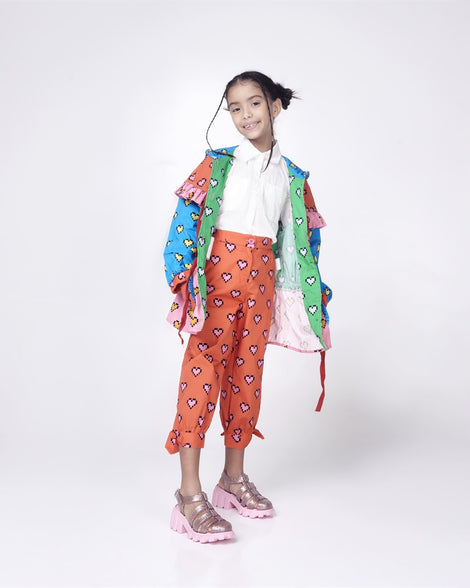 Child model in a white shirt, blue jacket and orange patterned pants wearing a pair of glitter pink Megan kids heel sandals.