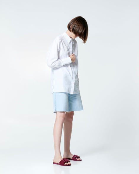 Model in jean shorts and white button down shirt wearing a pair of burgundy Babe slide sandals with large bow on top.