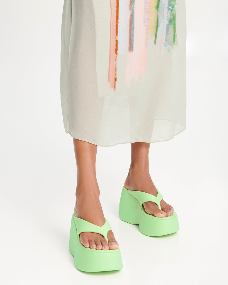 Model's legs wearing a pair of green Free Thong Wedge Platform heels
