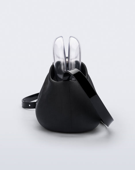 Side view of a small black bag with clear clutch and long strap