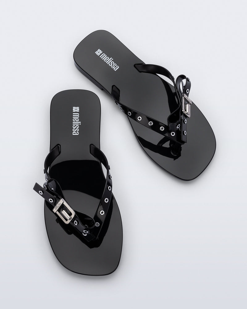 Top view of a pair of black Harmonic Squared flip flops with bow on strap