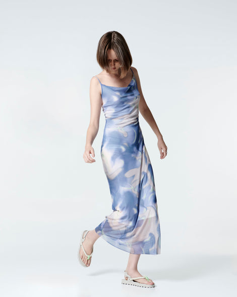 Model in a blue and white dress wearing a pair of beige Bond sandals with textile strap and green toe piece