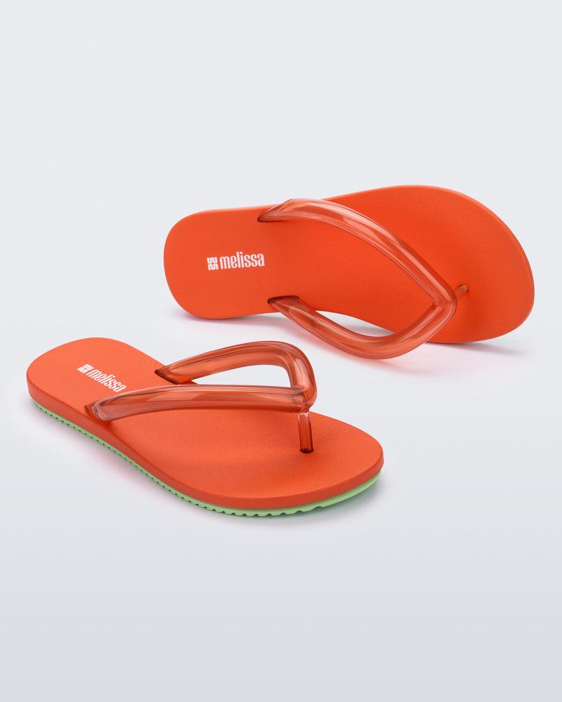 Top and angled view a pair of orange Flip Flop Airflow sandals with a clear orange strap and green bottom