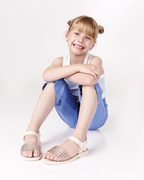 Child model in a white and blue tank top and blue capris wearing a pair of beige Mar Wave kids sandals.