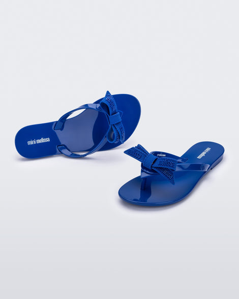 Top and angled view of a pair blue Harmonic M Lover kids flip flops with rainbow Melissa logo on bow