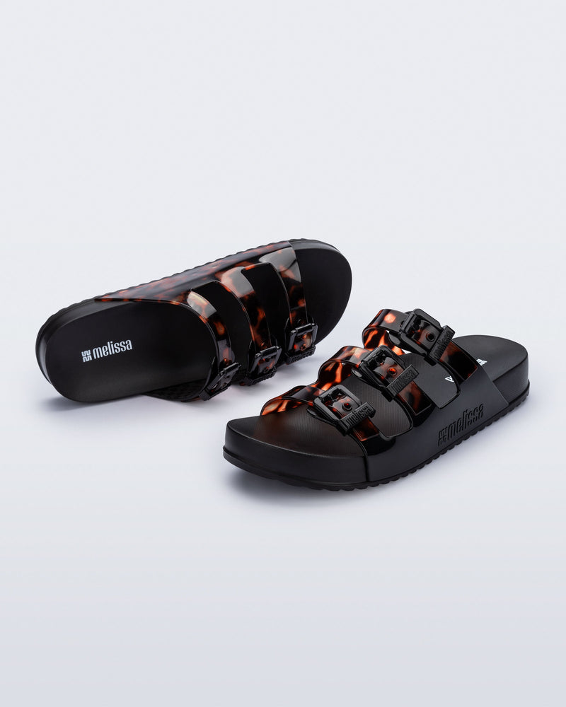 Top and angled view of a pair of black Cozy Stripes slides with tortoise colored straps
