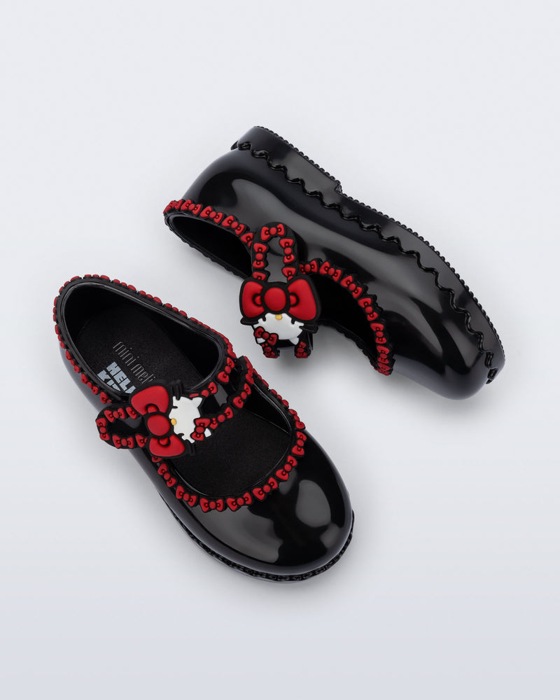 Top and side view of a pair of black Hip Ballerina + Hello Kitty baby flats with red trim