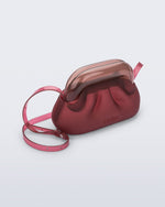 Angled view of a small red bag with clear brown clutch and long strap