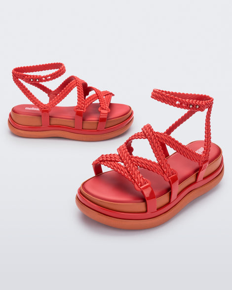 An angled front and side view of a pair of red Melissa Buzios platform sandals with multiple textured straps that mimic sisal braids across the front of the shoe as well as an ankle strap