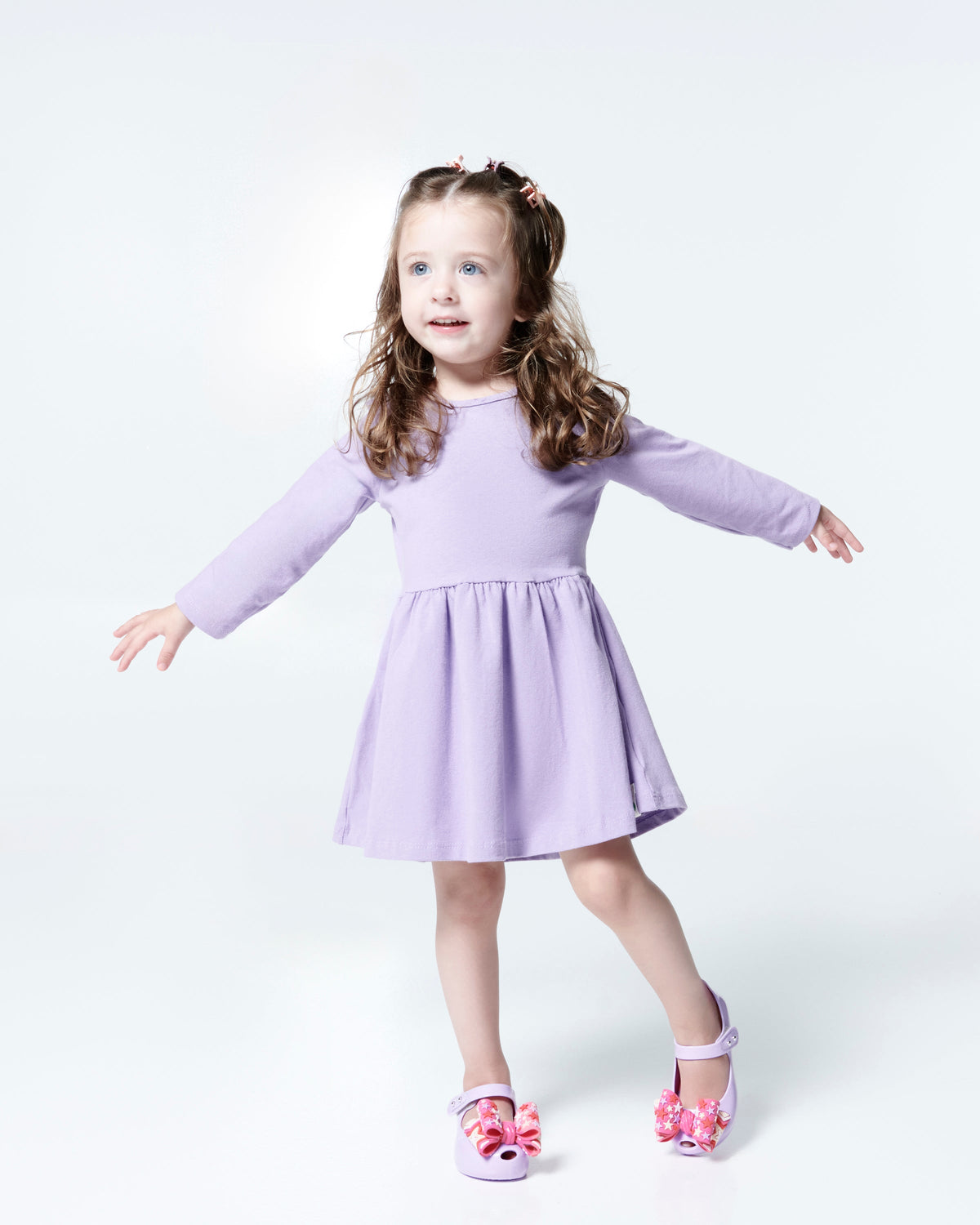 Child model in a lilac dress wearing a pair of lilac with pink star patterned bow Ultragirl Wonderland baby flats