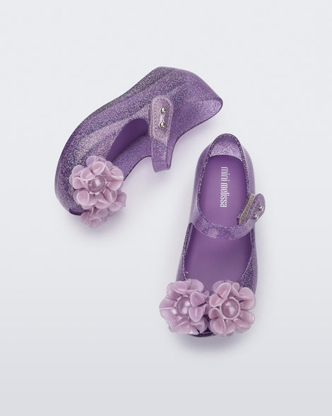 Side and top view of a pair of clear purple glitter Ultragirl Springtime baby flat with two purple flowers and peep toe.