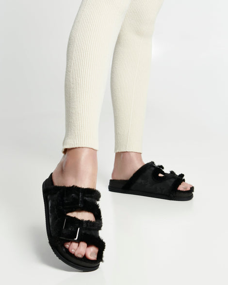 Model's legs in cream leggings wearing a pair of black Cozy Warm Slides with black fuzzy insoles