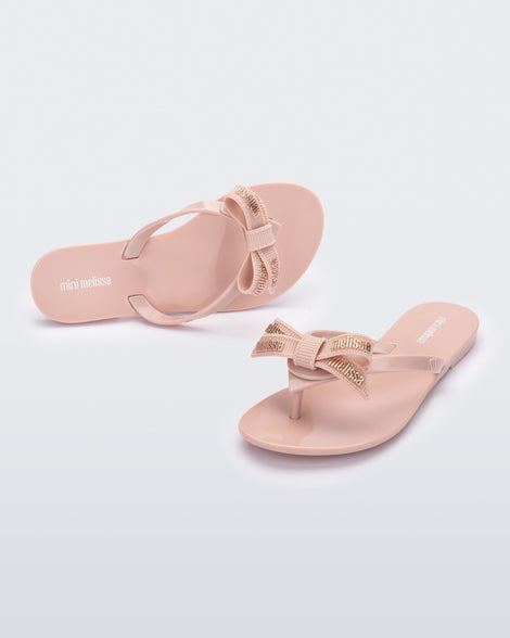 Top and angled view of a light pair pink Harmonic M Lover kids flip flops with rainbow Melissa logo on bow