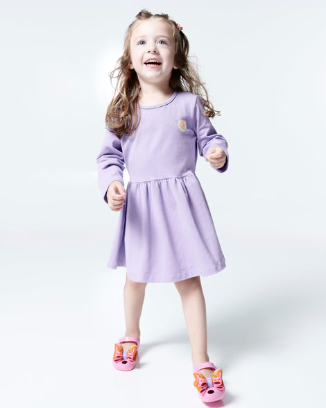 Child model in a lilac dress wearing a pair of pink with multi-colored patterned bow Ultragirl Wonderland baby flats