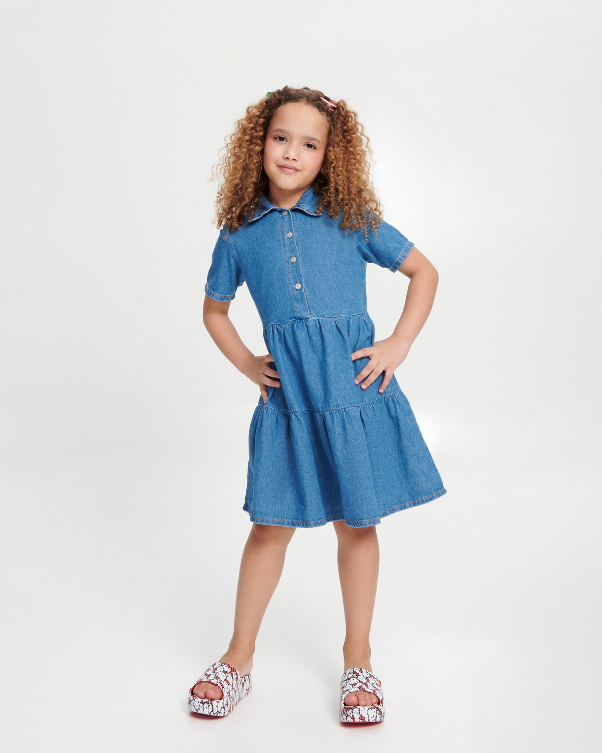 Child model in a blue dress wearing a pair of red Free Platform slides + Hello Kitty and Friends kids sandals with Hello Kitty print