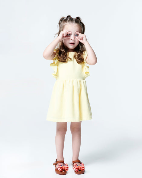 Child model in a yellow dress wearing a pair of brown with orange star patterned bow Ultragirl Wonderland baby flats