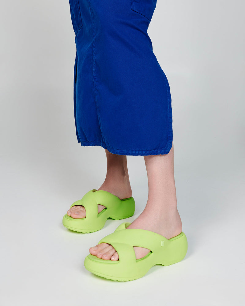 Model's legs in a blue skirt wearing a pair of green Free Rise platform slides