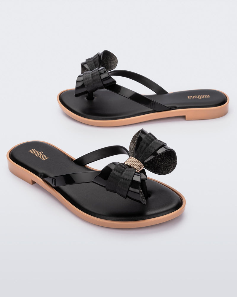 Angled view of a pair of Melissa slim strap flip flops in black with bow applique