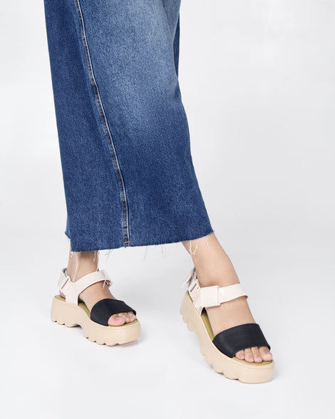 A model's legs in a denim skirt, wearing a pair of Beige/Black Melissa Kick Off Platform Sandals with a brown sole and two black and tan straps.