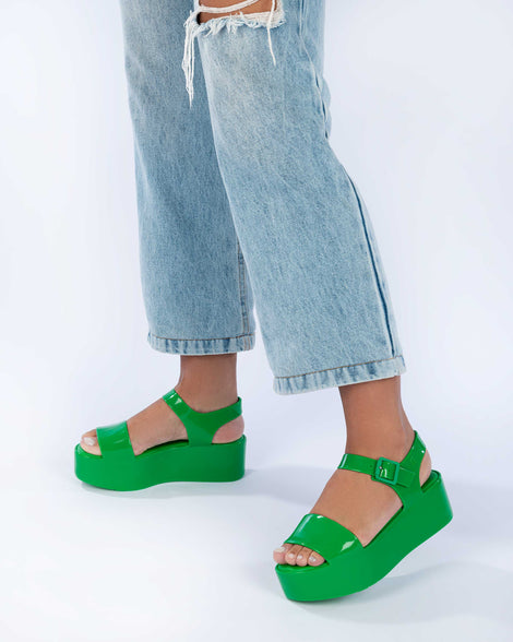 A model's legs wearing jeans and a pair of green Melissa Mar Platform sandals with two straps.