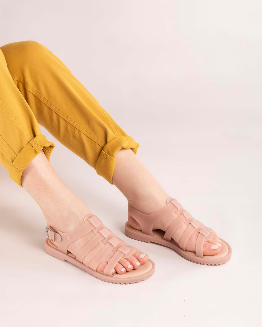 A model's legs wearing a pair of beige Melissa Flox sandals with straps.