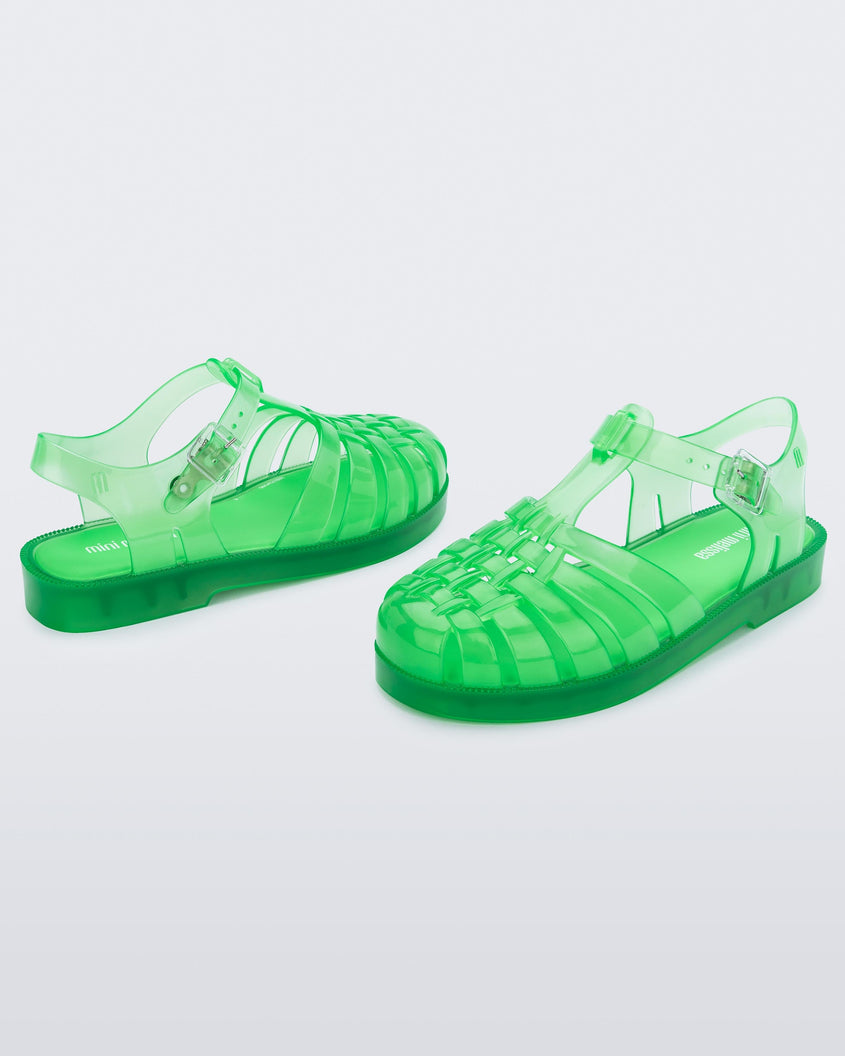 An angled front and back view of a pair of clear green Mini Melissa Possession sandals with several straps, a closed toe front and a back ankle strap.