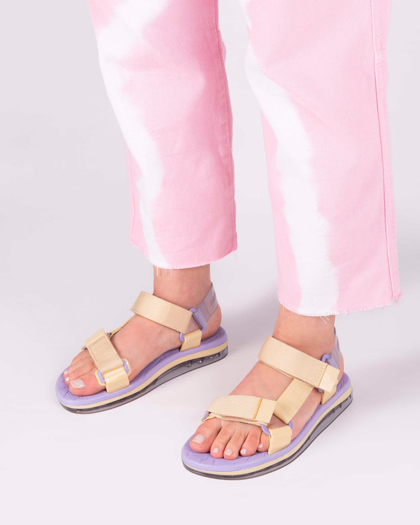 A model's legs wearing purple soled Melissa Papete sandals with yellow and transparent purple straps.