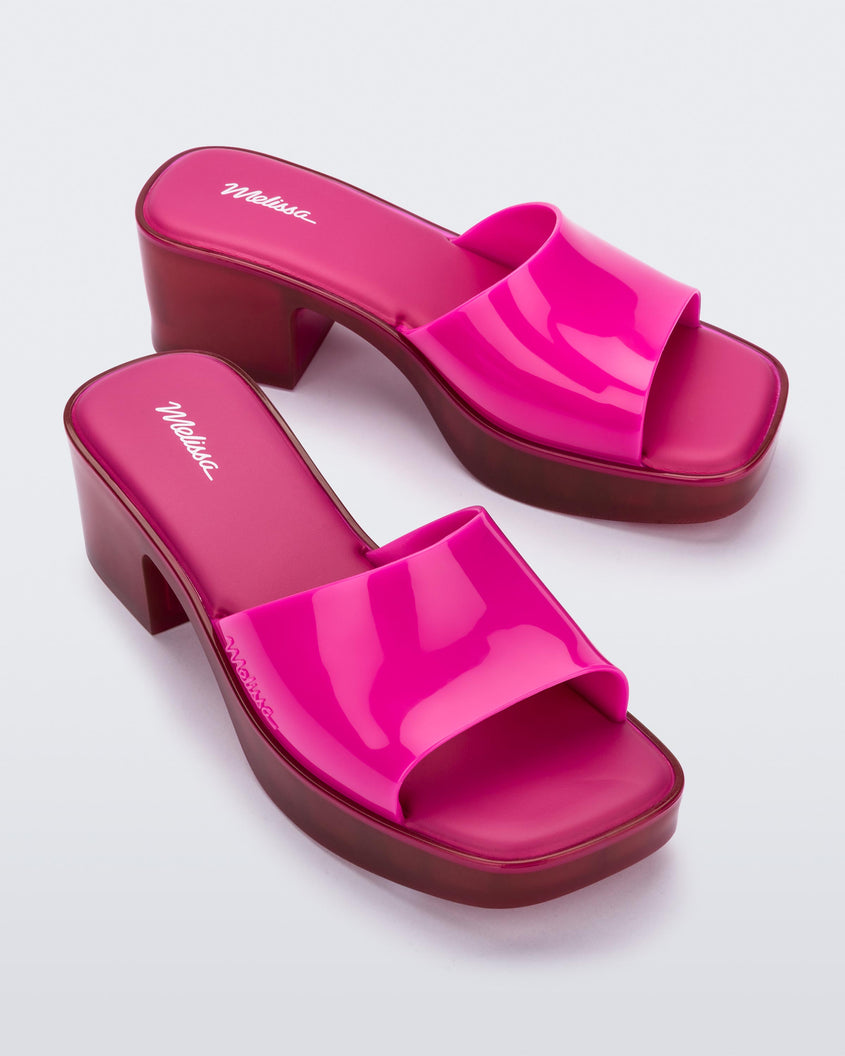 Side angle view of a pair of Melissa Shape slides with transparent pink platform heel and a hot pink wide front strap.