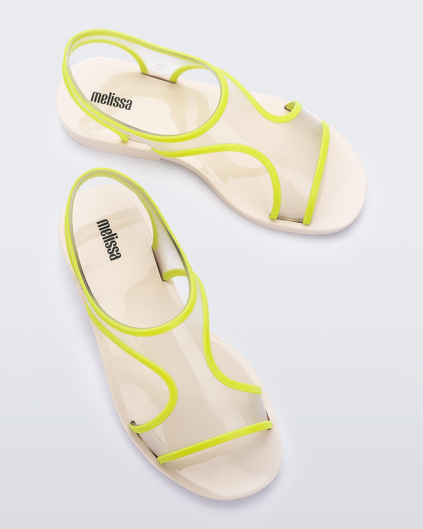 An angled top view of a pair of beige/green Melissa Bikini sandals with two transparent green straps conjoining in the middle and a beige insole.