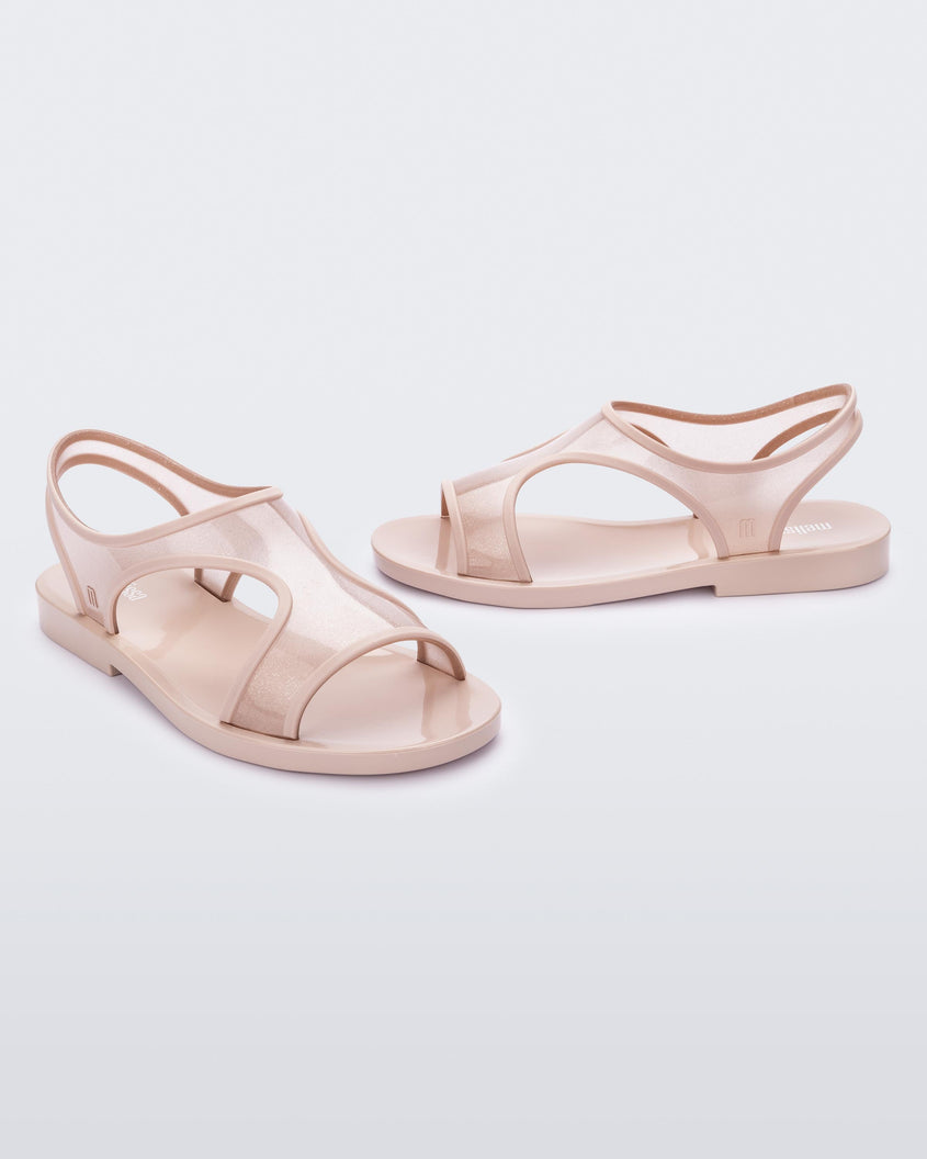An angled side and front view of a pair of transparent pink glitter Melissa Bikini Sandals with two transparent pink glitter straps conjoining in the middle and a pink insole.
