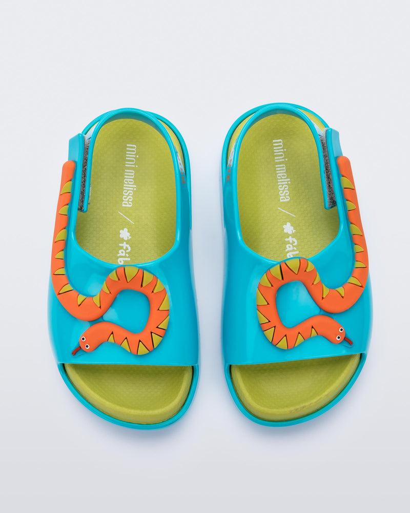 Top view of a pair of blue/green Mini Melissa Cloud sandals with a velcro back strap, a green insole, blue base and orange snake detail on the front.
