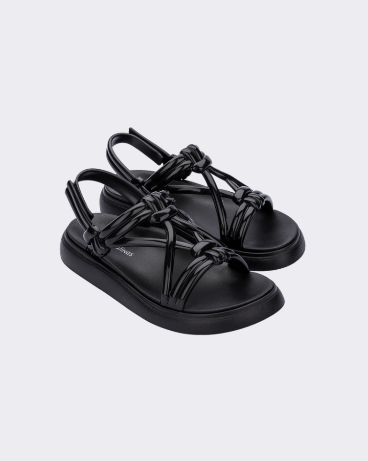 An angled front and side view of a pair of black Melissa Papete Essential sandals with straps.