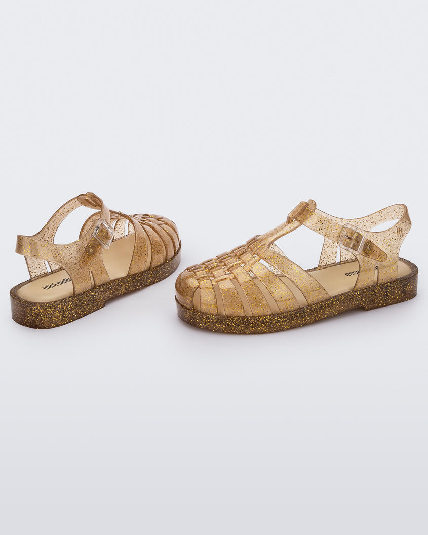 A side and back view of a pair of Beige/Glitter/Gold Mini Melissa Possession Shiny sandals with several straps and a gold glitter base.