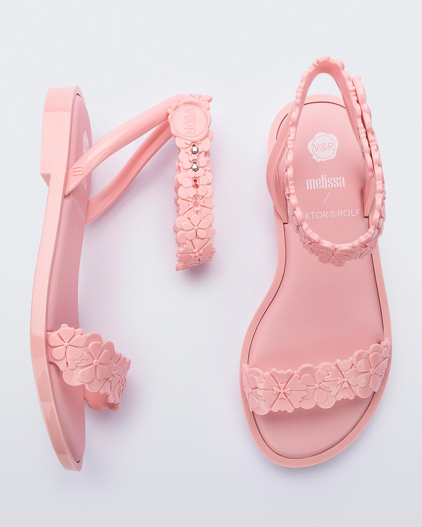 Top and side view of a pair of Melissa Wave Blossom sandals in pink with floral design ankle and front straps and double snap closure