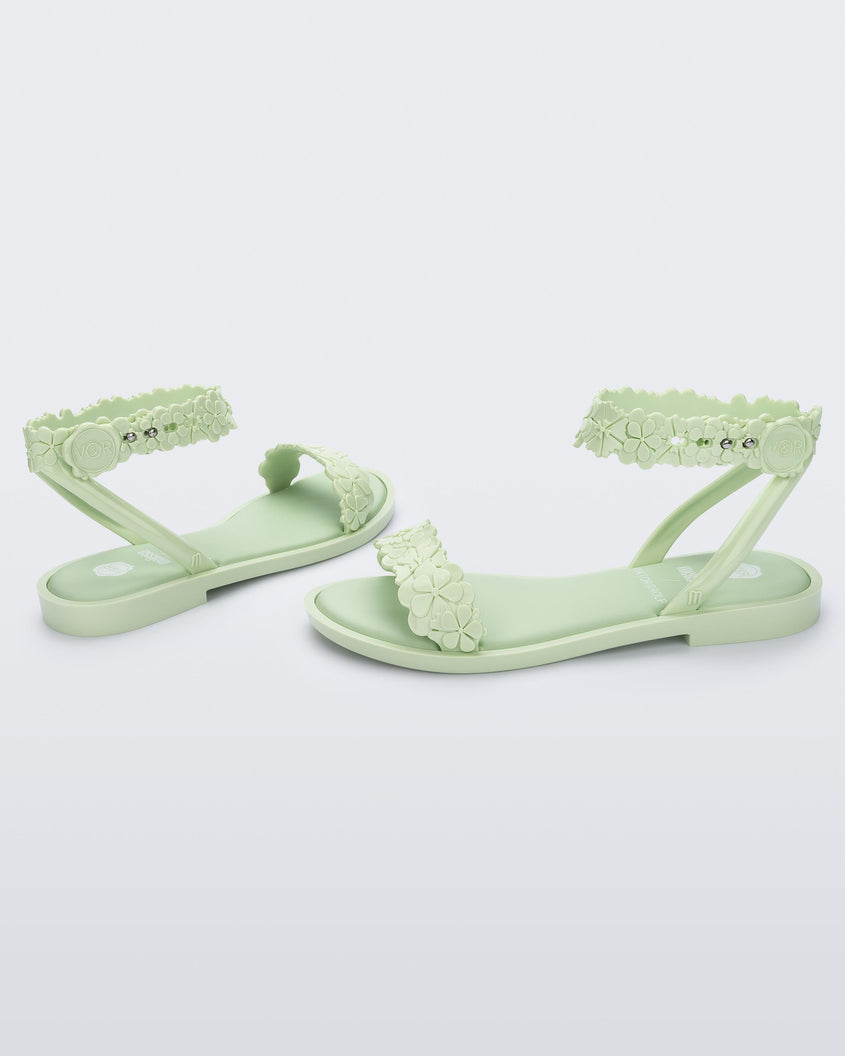 Angled view of a pair of Melissa Wave Blossom sandals in Green with floral design ankle and front straps and double snap closure