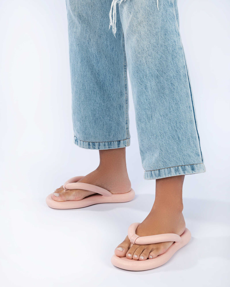 A model's legs wearing a pair of light pink Melissa Free Flip Flops with puffer-like straps.
