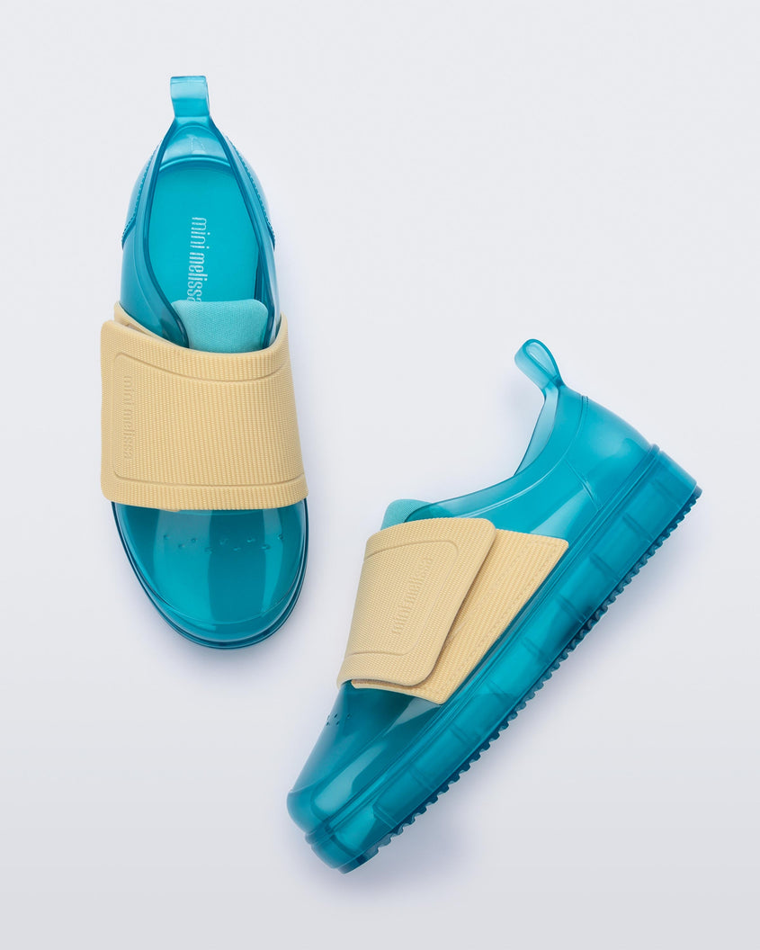 A top and side view of a pair of blue/yellow Mini Melissa Jelly Pop Sneakers with a blue base and a yellow velcro strap.