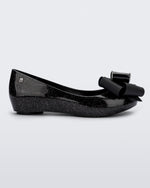 Side view of the Melissa Ultragirl ballet flat in black glitter. There is a silver M located on the back heel. The front toe of the flat has a 3D Bow applique