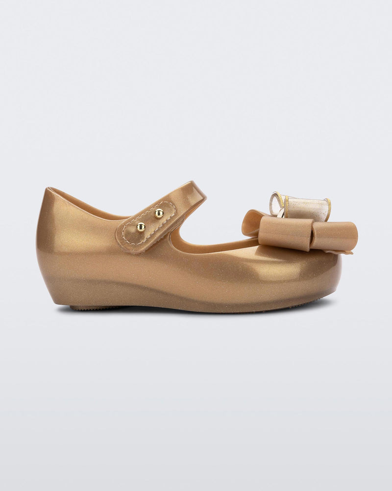 Side view of a gold Mini Melissa Ultragirl Sweet flat with a top strap and a bow detail on the toe.