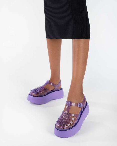 A model's legs wearing a black skirt and a pair of a lilac Melissa Possession Platform sandals with several straps and a closed toe front.