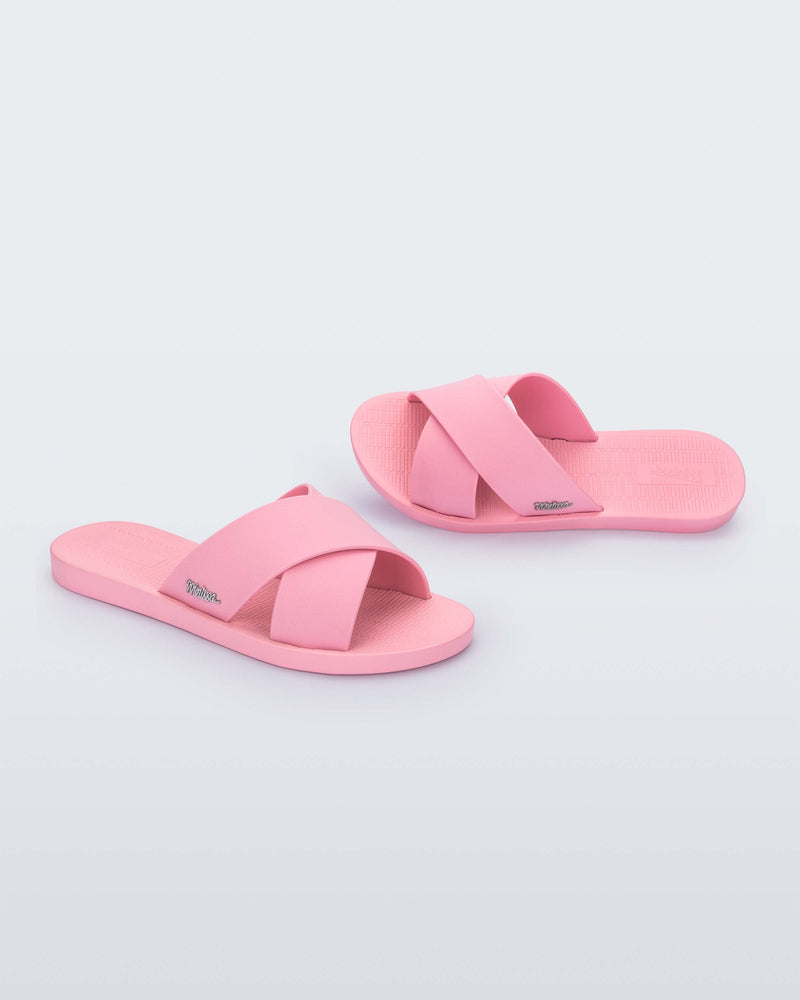 A side and top view of a pair of pink Melissa Sun City Walk slides with a melissa logo on the side and two overlapping straps.