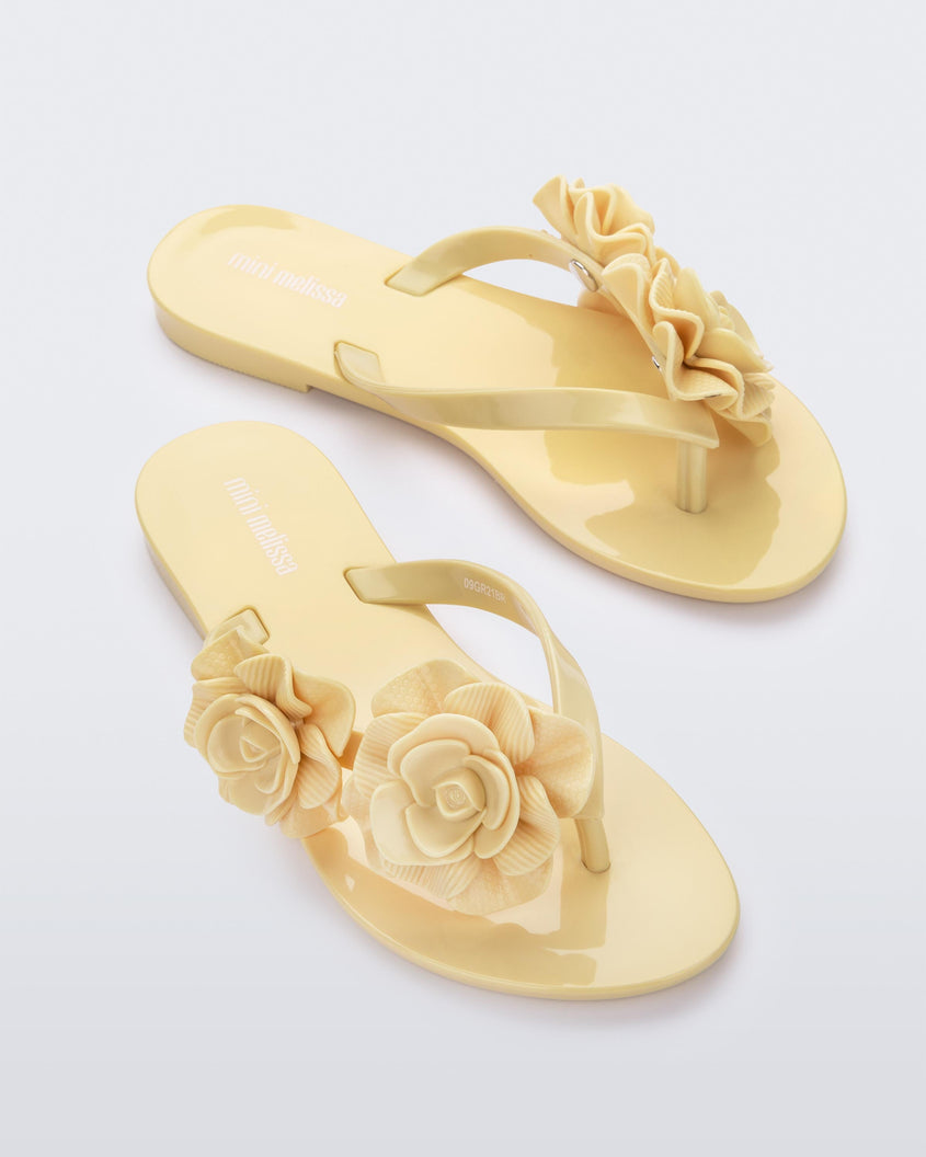 An angled top view of a pair of yellow Harmonic Garden flip flops with flowers on the straps.
