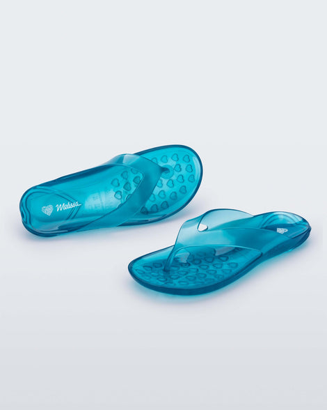 An angled front and top view of a pair of clear blue Melissa Real Jelly Flip Flops.