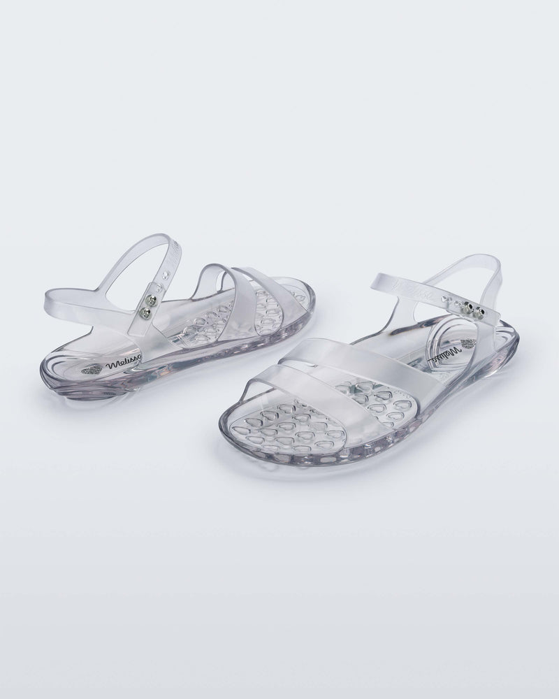 An angled front and side view of a pair of clear Melissa Real Jelly Sandals with two front straps and an ankle strap.